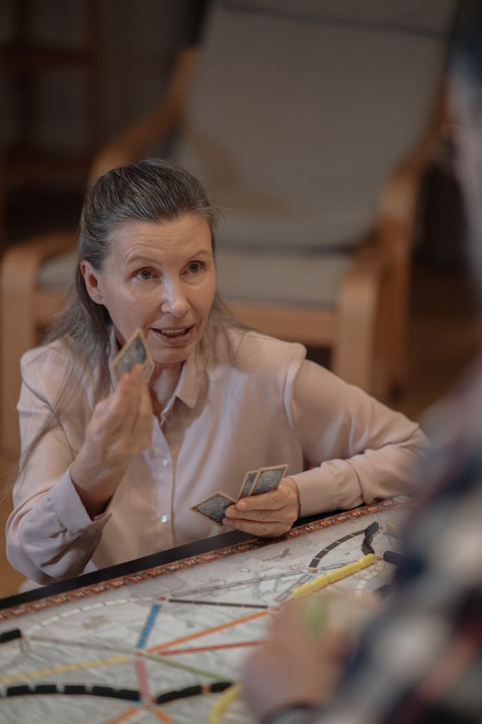 Elderly woman playing cards in a cozy indoor setting, enjoying leisure time.