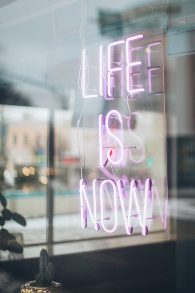 Urban scene with a glowing Life is Now neon sign reflecting in a window, conveying a modern, motivational vibe.